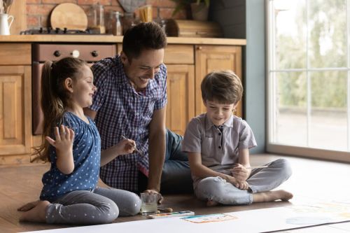 Caring dad drawing with two small kids at home, child custody after successful mediation.