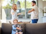Kid feeling upset while parents argue in room. Couple arguing is showing signs of parental alienation.