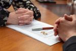 Divorce signature, marriage dissolution document. Wedding ring and agreement on lawyer office table — alimony modification concept.