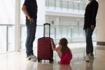 Man and woman stand at distance from each other in middle of child with a suitcase