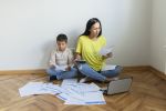 Stressed Young Family Mother and Son Looking So Many Expenses Bills Such as Electricity Bill, Water Bill, Internet Bill, Cell Phone Bill and Credit Card Bill in His Hand No Money to Pay Debt. Mother Managing Domestic Budget Together in Empty Apartment While Her Son Sitting Next to Her